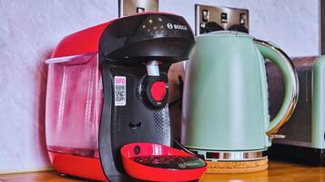 Una cafetera roja y negra con un código QR y un hervidor verde sobre una superficie de madera.