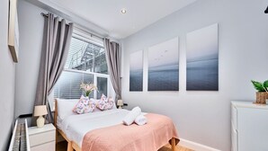Un dormitorio con cama, mesita de noche, cómoda y ventana con cortinas.
