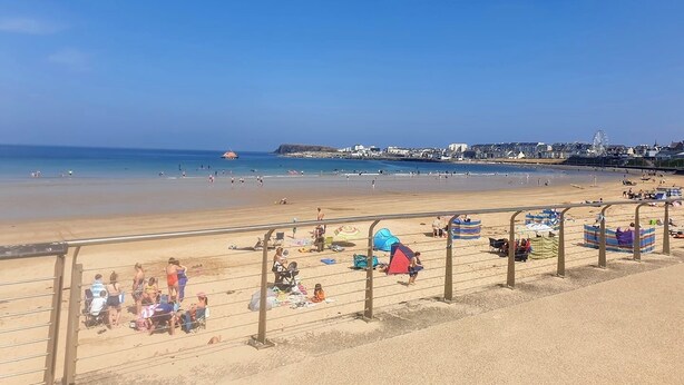 Una playa con cielo despejado, orilla de arena y un horizonte con edificios de la ciudad.