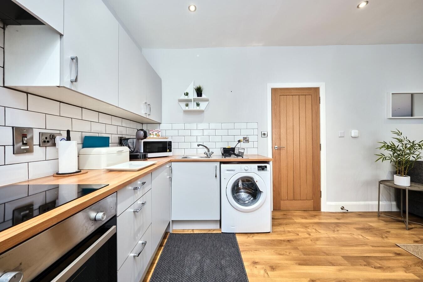 Une cuisine de taille réduite avec des meubles blancs, un four à micro-ondes, un lave-linge et un plan de travail en bois.
