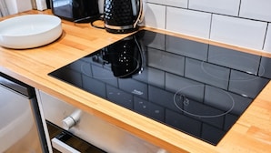 Una cocina moderna con una placa de inducción negra, un bol blanco y una cafetera sobre la encimera.