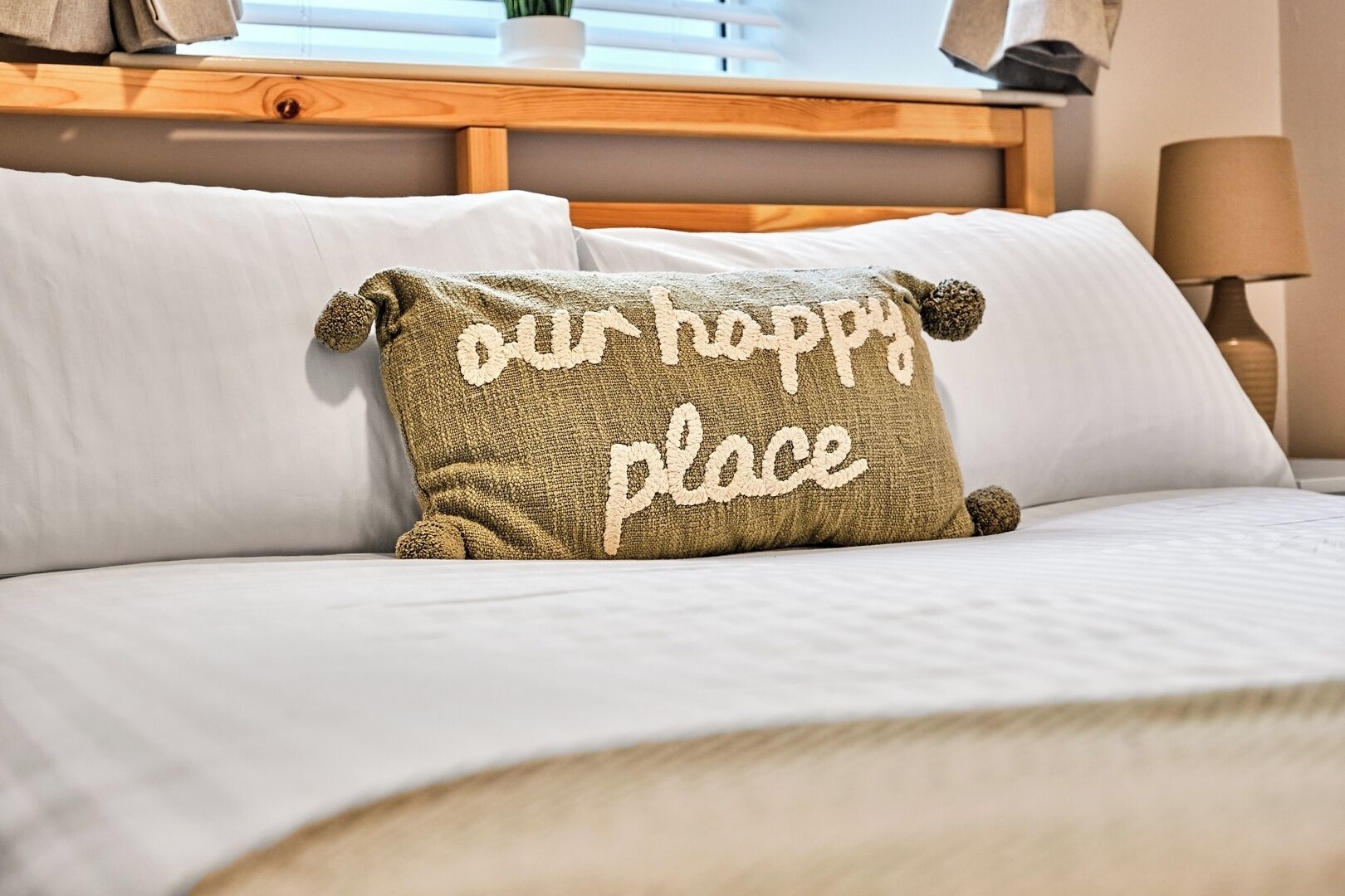 A bed with white linens and a pillow with the text "our happy place".