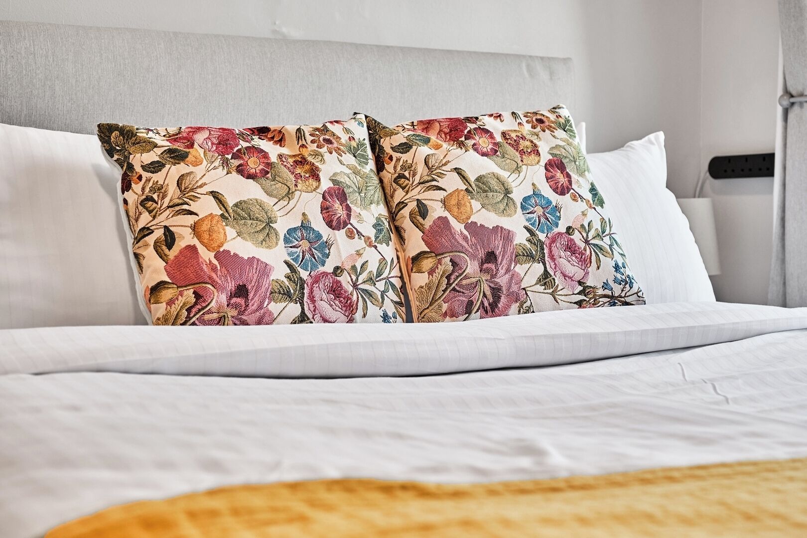 Una cama bien hecha con sábanas blancas y dos almohadas decorativas con estampado floral.