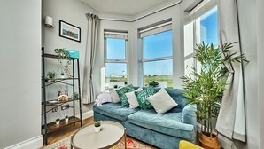 A modern living room with a blue sofa, a small round table, and a bookshelf with plants. - Bright Apt Steps From the Beach (Portrush)