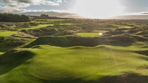 A golf course with undulating terrain and a flag on the green. - Bright Apt Steps From the Beach (Portrush)