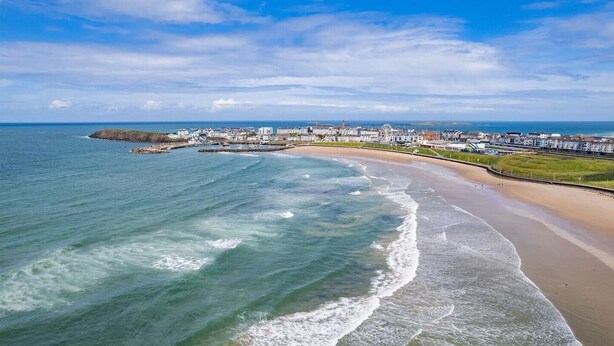 An aerial view of a coastal town with a beach, buildings, and a pier. - Bright Apt Steps From the Beach (Portrush)
