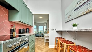 A modern kitchen with a stove, cabinets, and a dining area with stools. - Bright Apt Steps From the Beach (Portrush)