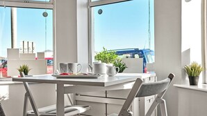 A modern dining area with a white table and chairs, a window with a view of the city, and a small potted plant on the windowsill.