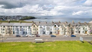 A row of terraced houses along a coastal road with a view of the sea. - Victorian Apartment Steps to Beach (Portrush)