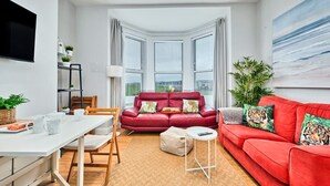 A modern living room with a red sofa, a white coffee table, and a red couch. There is a dining table with chairs and a plant on the left. - Victorian Apartment Steps to Beach (Portrush)