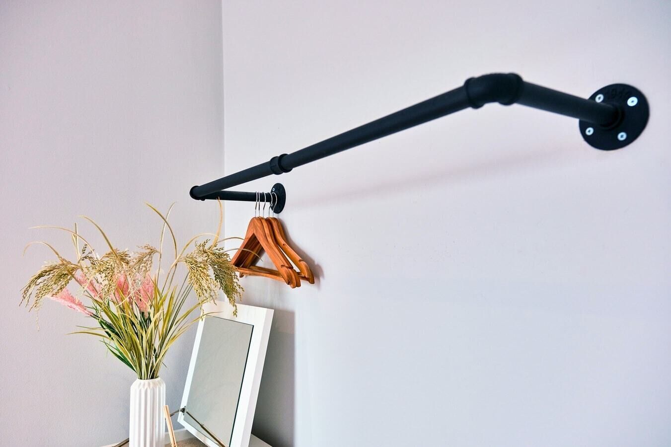 Eine schwarze Wandlampe mit einer weißen Vase, in der Pflanzen stehen, und einem gerahmten Bild.