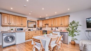 A modern kitchen with wooden cabinets, a dining table with chairs, a washing machine, and a large potted plant. - Spacious Bright Apt Walk to the Beach (Portrush)