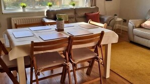A dining area with a table and chairs, a window with plants, a sofa, and a framed picture on the wall. - Spacious Bright Apt Walk to the Beach (Portrush)