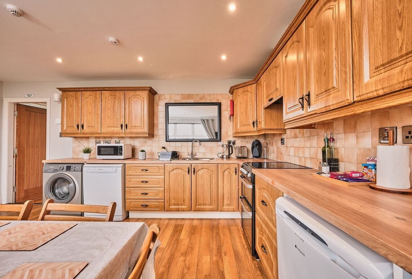 Una cucina funzionale con mobili in legno, un forno a microonde, una lavatrice ed una lavastoviglie.