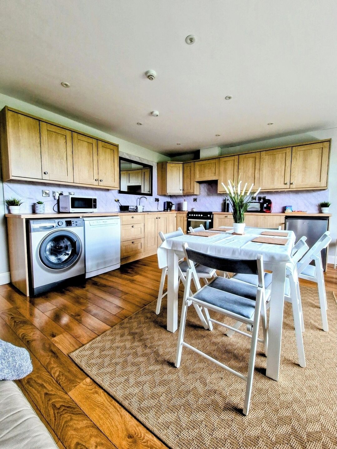 A modern kitchen with wooden cabinets, a washing machine, a dining table with chairs, and a small dining area.