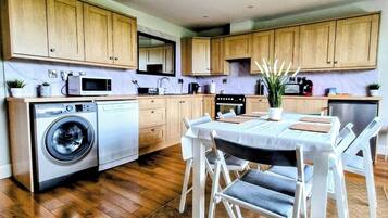 A modern kitchen with wooden cabinets, a washing machine, a dining table with chairs, and a small dining area.