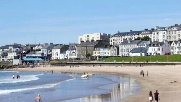 A beach with people walking and standing, a clear sky, and buildings in the background. - Spacious Bright Apt Walk to the Beach (Portrush)