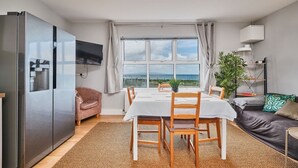 A modern kitchen with a built-in refrigerator, a dining area with a table and chairs, and a view of the sea through large windows. - Panoramic Sea View Beach Apartment (Portrush)