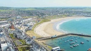 An aerial view of a coastal town with a sandy beach, a marina with boats, and a prominent pier. - Panoramic Sea View Beach Apartment (Portrush)