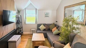 Un salon moderne avec un canapé d’angle, un téléviseur, un plancher en bois et un grand miroir.