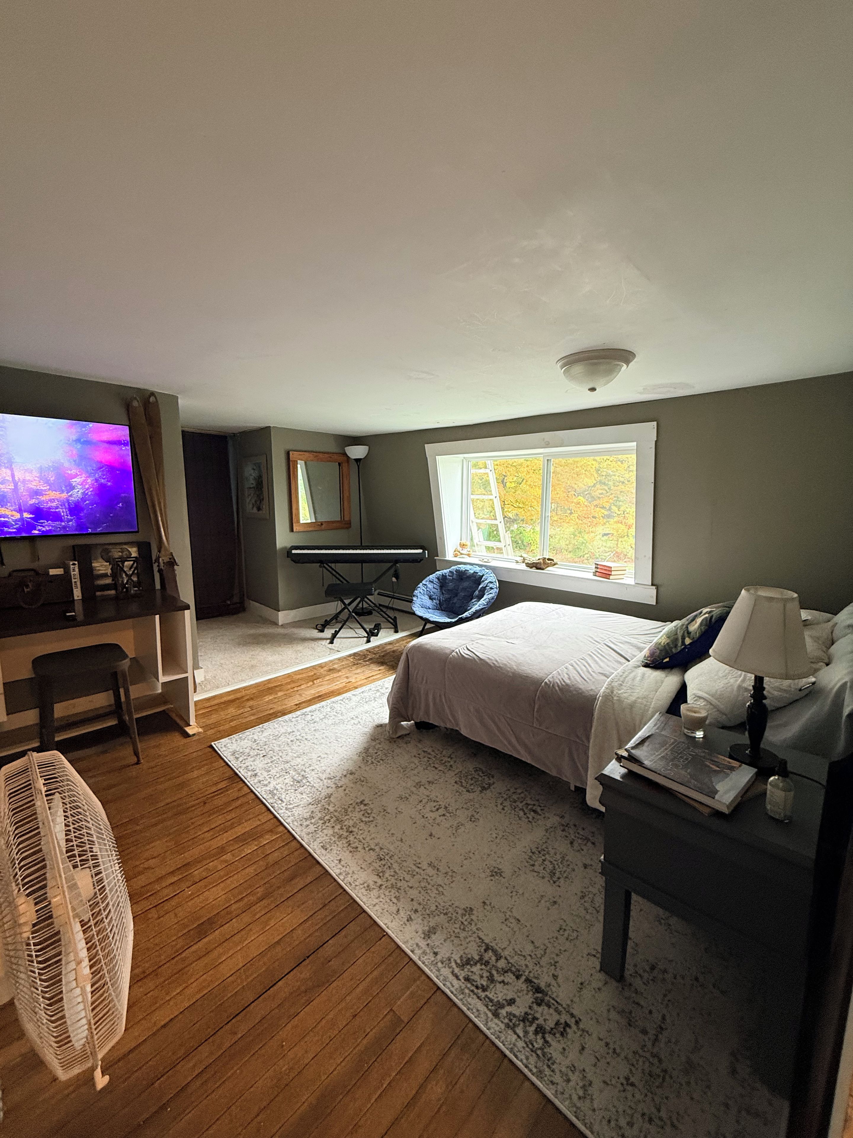 A bedroom with a bed, bedside table, lamp, and a desk with a chair.