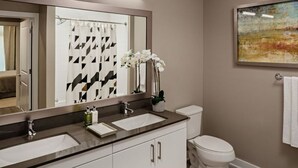 A modern bathroom with two sinks, a toilet, and a large mirror. - Kings Point Lux Suites (Great Neck)