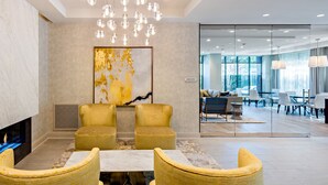 A modern lobby with a fireplace, two yellow armchairs, a marble wall, and a large abstract painting. - Kings Point Lux Suites (Great Neck)