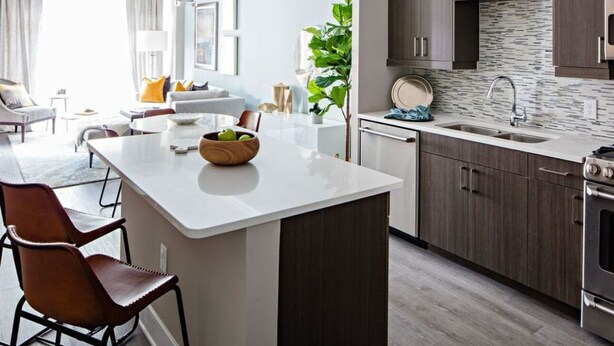 A modern kitchen with dark wood cabinets, a white countertop, and a built-in stove. - Kings Point Lux Suites (Great Neck)