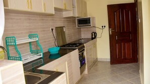 Une cuisine compacte équipée d’un four à micro-ondes, d’une cuisinière et d’un évier. On y trouve un égouttoir à vaisselle de couleur turquoise et une porte en bois.