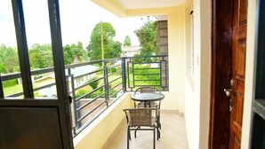 Un balcon avec une table et des chaises, une vue sur la verdure et les bâtiments, et une porte en bois.