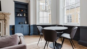 A room with a round table and four chairs, a blue cabinet with shelves, and a large window with a view of buildings.