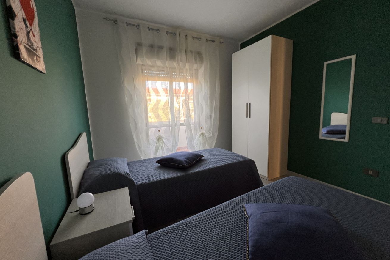 Une chambre avec deux lits, une armoire, un miroir et une fenêtre avec des rideaux.
