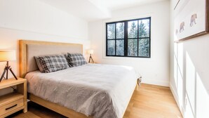 A bedroom with a bed, bedside tables, a window with a view of trees, and a wall-mounted artwork. - Golden Hour: 3-bedroom luxury home in the Canadian Wilderness (Golden)