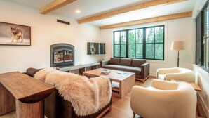 A cozy living room with a fireplace, a large window, and a wooden ceiling. - Golden Hour: 3-bedroom luxury home in the Canadian Wilderness (Golden)