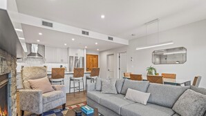 A modern living room with a grey sofa, a fireplace, and a kitchen in the background. - Spring Creek Vacations 2 BR Premier Condo 109TM (Canmore)