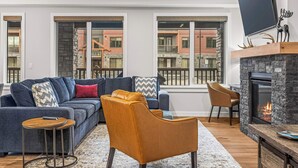 Una sala de estar moderna con un sofá seccional, una chimenea y ventanas amplias que ofrecen vistas de la ciudad.