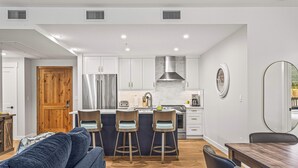 Una cocina moderna con armarios blancos, electrodomésticos de acero inoxidable y una isla central con taburetes de bar.