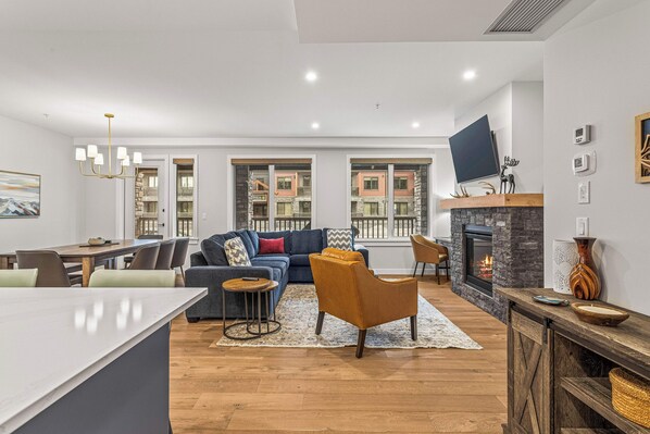 Un salon moderne avec un canapé, un fauteuil et une cheminée. On y trouve également un coin repas avec une table et des chaises.