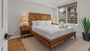 Ein Schlafzimmer mit einem hölzernen Bett, zwei Nachttischen, einem großen Fenster mit Bergblick und einem Topfpflanzen.
