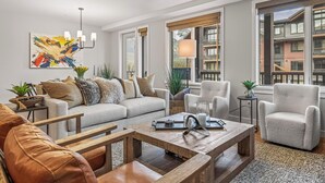 Ein modernes Wohnzimmer mit einer Couch, Sesseln, einem Couchtisch und einem großen Fenster mit Blick auf Gebäude.