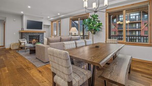 A spacious living room with a fireplace, a large TV, and a dining area with wooden furniture. - Spring Creek Vacations 3 BR Premier Condo 213TM (Canmore)