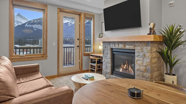 A cozy living room with a fireplace, a sofa, a coffee table, and a TV mounted on the wall. - Spring Creek Vacations 1 BR Condo 211TM (Canmore)