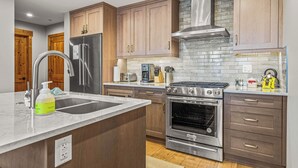 A modern kitchen with wooden cabinets, stainless steel appliances, and a marble countertop. - Spring Creek Vacations 1 BR Condo 211TM (Canmore)