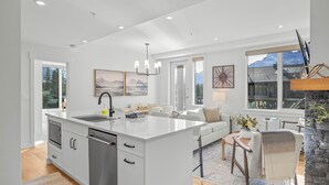 A modern kitchen with a large island, white cabinetry, and a stone fireplace. - Spring Creek Vacations 2 BR Premier Condo 304TM (Canmore)