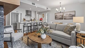 A modern living room with a grey sofa, a wooden coffee table, and a kitchen in the background. - Spring Creek Vacations 2 BR Premier Condo 304TM (Canmore)