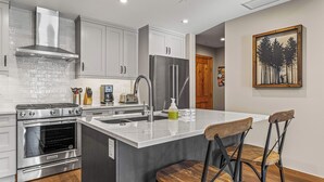 Una cocina moderna con electrodomésticos de acero inoxidable, una isla grande con taburetes de bar y un cuadro en la pared.