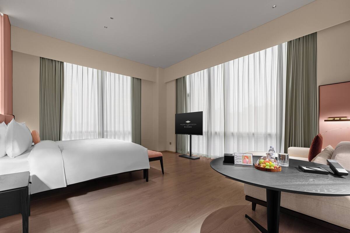 A modern hotel room with a bed, a desk, a chair, and a TV.