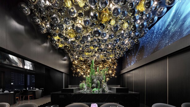 Interior de restaurante moderno con un diseño de techo original, un arreglo floral central y vistas de la ciudad a través de amplios ventanales.