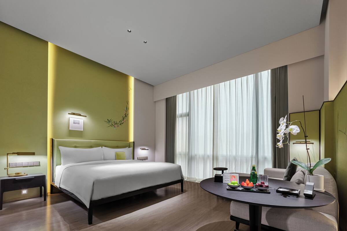 A modern hotel room with a bed, bedside tables, a desk, and a dining area.