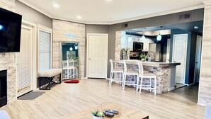 A modern living room with a fireplace, a TV, and a dining area with a kitchen in the background. - Modern North Scottsdale Condo – Resort Style Amenities, 1st Floor Corner Unit (Scottsdale)